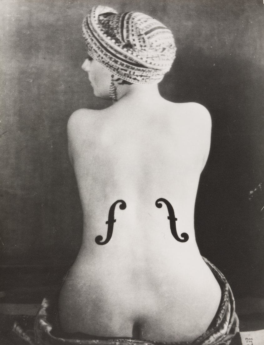 Man Ray, Kiki, Violon d’Ingres, 1924, Gelatinesilberpapier, Montage 38,6 x 30 cm, Museum Ludwig, Köln, Repro: Historisches Archiv der Stadt Köln mit Rheinischem Bildarchiv, © Man Ray 2015 Trust / VG Bild-Kunst, 2026 Ein schwarz-weiß Foto zeigt einen einen nackten Rücken einer Frau. Um die Hüfte und um den Kopf trägt sie ein Tuch. Auf das Foto sind Schalllöcher einer Geige gemalt.