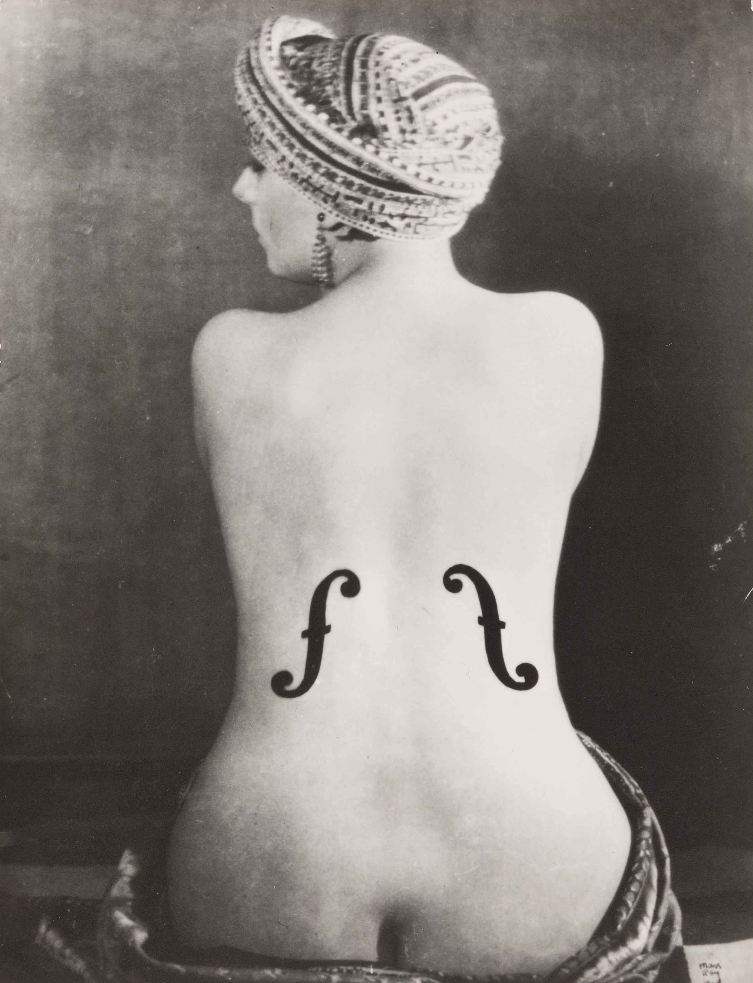 Man Ray, Kiki, Violon d’Ingres, 1924, Gelatinesilberpapier, Montage 38,6 x 30 cm, Museum Ludwig, Köln, Repro: Historisches Archiv der Stadt Köln mit Rheinischem Bildarchiv, © Man Ray 2015 Trust / VG Bild-Kunst, 2026 Ein schwarz-weiß Foto zeigt einen einen nackten Rücken einer Frau. Um die Hüfte und um den Kopf trägt sie ein Tuch. Auf das Foto sind Schalllöcher einer Geige gemalt.