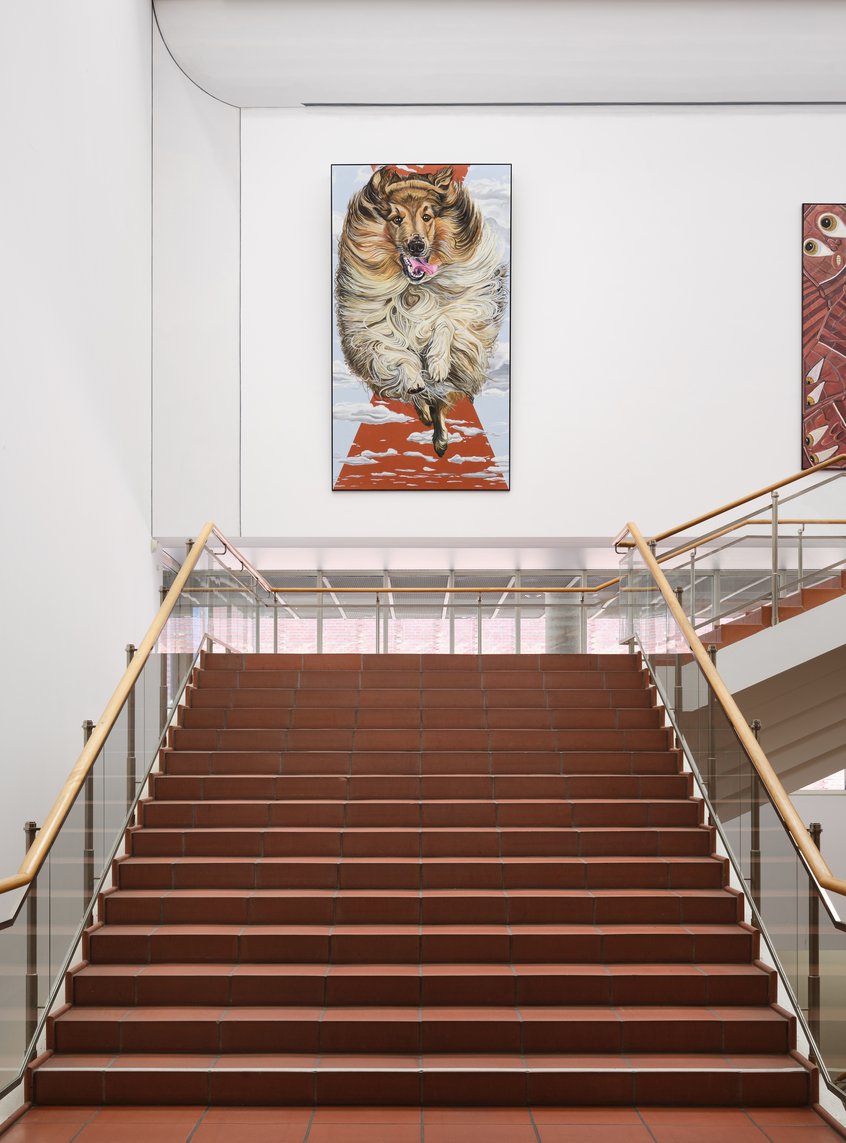 Jana Euler, One on One, Triptych – Image Viewer Connections, 2026, Schultze Projects #5, Museum Ludwig, Köln, © Jana Euler, Foto: Historisches Archiv der Stadt Köln mit Rheinischem Bildarchiv/Marc Weber Blick auf eine rot-braune Treppe, an der weißen Wand drüber hängt ein großformatiges Kunstwerk: ein Gemälde eines Langhaar Collies, der auf die Betrachter*innen zuzulaufen scheint, ist zu sehen.